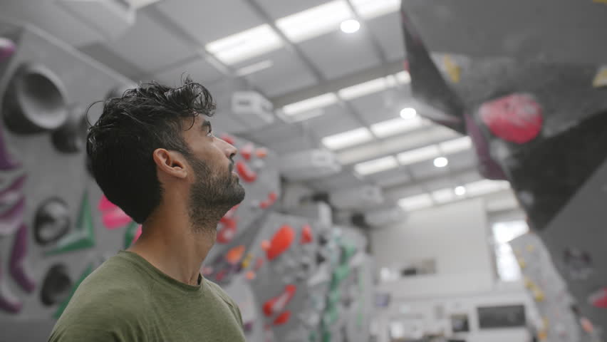 Portrait Of Smiling Male Coach Standing In Front Of Climbing Wall At Indoor Centre
