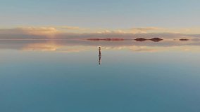 Aerial of a lone figure standing on the mirrored reflection of the world's largest salt flat in the Uyuni Salt Flats (Salar de Uyuni), Bolivia. Drone tracking pan shot - Powered by Shutterstock - Get 15% off with code: PIKWIZARD15