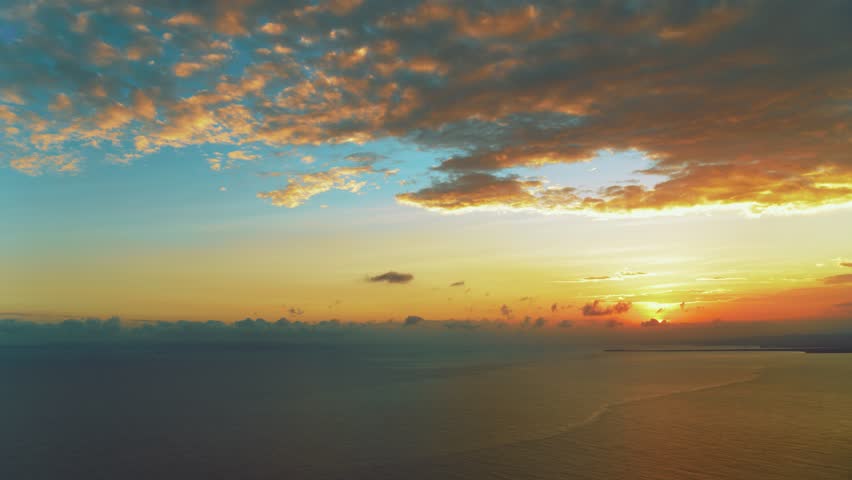 Orange sunset over turquoise sea on a tropical summer evening. Sea waves with sunset reflections. Calm sea water. Blue ocean under a turquoise sky with orange clouds. Twilight over the sea.