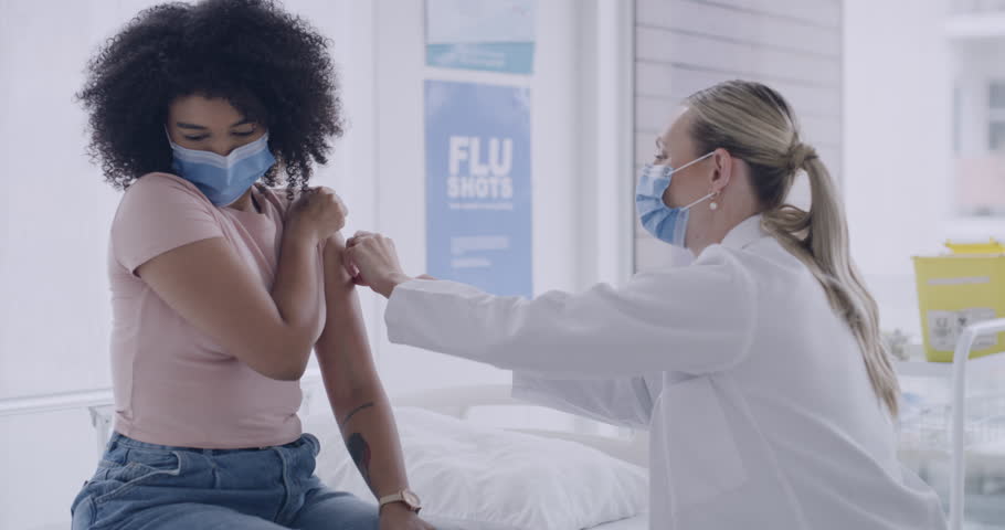 A female doctor wearing a mask injecting the patient with the coronavirus vaccination. An African-American confident woman taking the covid-19 vaccine and smiling after getting the dose in a clinic. Royalty-Free Stock Footage #1103436513