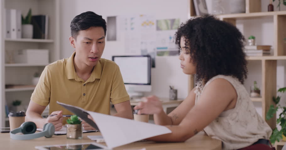Trendy business people discussing a project during a productive meeting. Young colleagues working and collaborating on a document together, brainstorming ideas for a creative marketing strategy