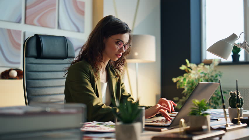 Focused business woman typing at modern laptop in office interior close up. Attractive young girl manager in glasses looking computer screen sitting desk. Serious woman company worker surfing internet Royalty-Free Stock Footage #1103439217