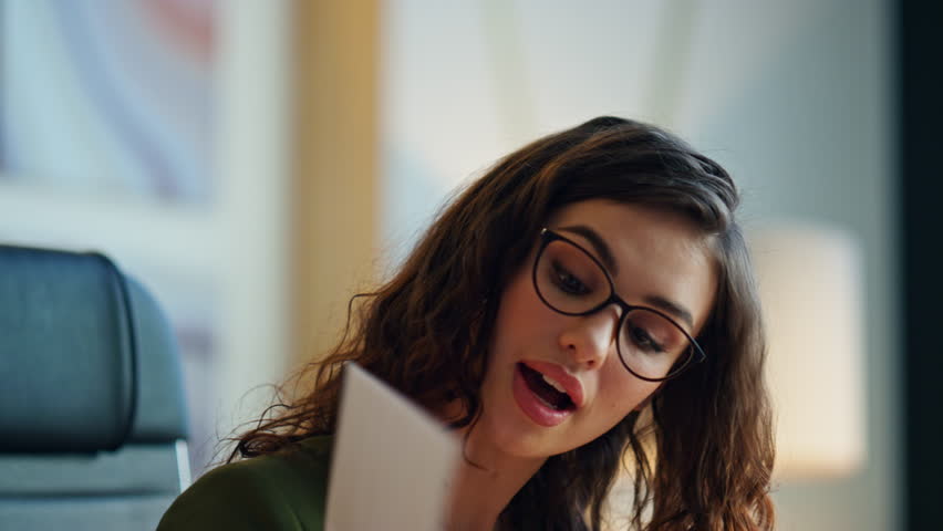 Creative woman designer presenting work on video call sitting office close up. Attractive young businesswoman showing work samples at online conference indoors. Elegant girl manager in glasses talking