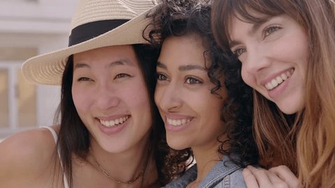 Close up portrait of three young smiling women laughing together outdoors. Diverse female friends having fun together on summer vacation. Youth lifestyle and friendship concept. Arkistovideo