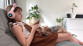 girl and her dog yorkshire terrier enjoy a cozy moment together. little cute caucasian girl in headphones studying on the phone with a dog, watching videos and writing messages