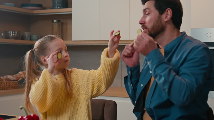 Caucasian father with little daughter at home kitchen cooking eating together child girl kid feed dad with cucumber slice daddy joking pretend feeding baby deceive cheat fooling around happy family Royalty-Free Stock Footage #1103454675