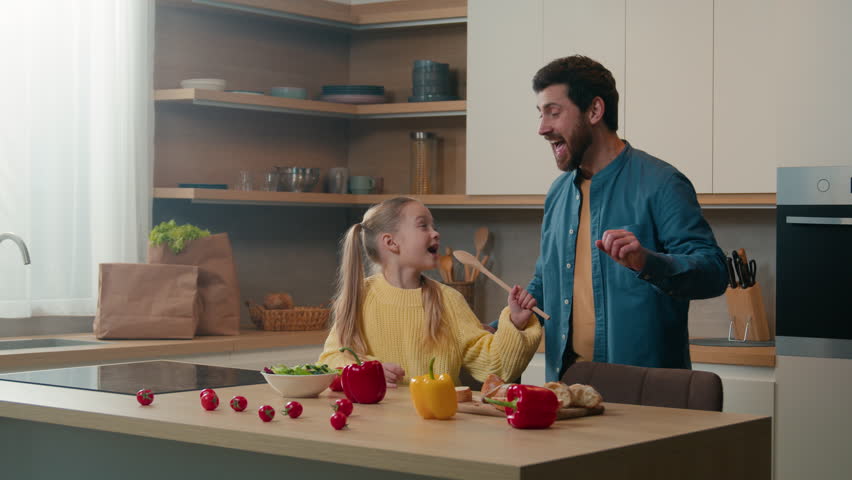 Happy family having fun at kitchen Caucasian father dancing funny active dance little daughter singing in spoon child girl sing song in kitchenware ladle microphone fooling around cooking together Royalty-Free Stock Footage #1103454685