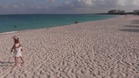 Aerial drone footage of woman in white walking with her baby on sandy beach near blue sea in Aruba island in Caribbean.