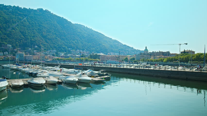 Beautiful boats and vessels by the port in Como, Italy. Summer sunny view of sailing boats stationary by the coast of Lake Como with turquoise water in Prores 4K.