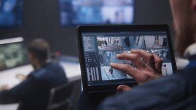 Close up shot of security operator zooming CCTV cameras with AI facial recognition using tablet in police surveillance center. Colleagues work at background. Monitoring system. Social safety concept. - Powered by Shutterstock - Get 15% off with code: PIKWIZARD15