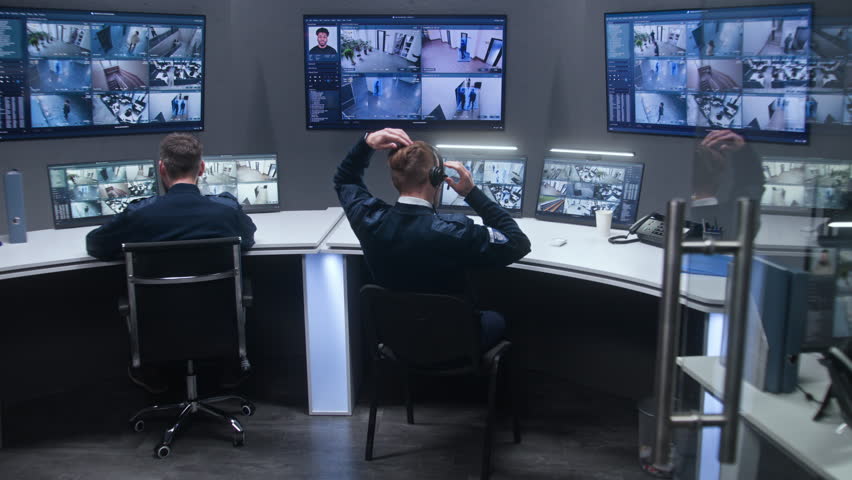 Diverse team of officers monitor CCTV cameras with AI face recognition. Employees work in security control center. Computer monitors and big digital screens showing surveillance cameras video footage. Royalty-Free Stock Footage #1103458789