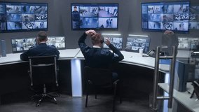Diverse team of officers monitor CCTV cameras with AI face recognition. Employees work in security control center. Computer monitors and big digital screens showing surveillance cameras video footage.