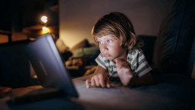 cheerful little boy in front monitor watching cartoons. Side view of child casual clothes sitting table netbook pc apartment. High-quality 4k horizontal footage time lapse