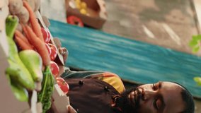 Vertical video: Portrait of man vendor selling box filled with bio tomatoes and advertising own homegrown products at local farmers market. Male farmer small business owner at food fair. Handheld shot - Powered by Shutterstock - Get 15% off with code: PIKWIZARD15