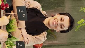 Vertical video: Portrait of woman farmer selling healthy products at local marketplace, showing seasonal eco fruits and vegetables at farmers market. Young vendor preparing to sell bio organic food. - Powered by Shutterstock - Get 15% off with code: PIKWIZARD15