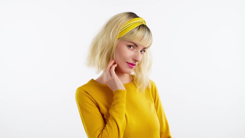 Woman sends air kiss smiling looking at camera. Happy positive emotional blonde girl. Joyful cheerful pretty lady in yellow sweater, smile face. Indoors studio, isolated on white background | Shutterstock HD Video #1103461231