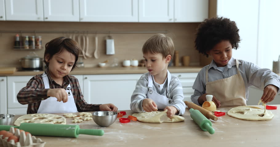Diverse team of boys cutting dough for cookies, biscuits, training culinary, baking skills, preparing sweet bakery snacks, pastry dessert for family holiday, talking at floury kitchen table Royalty-Free Stock Footage #1103465969