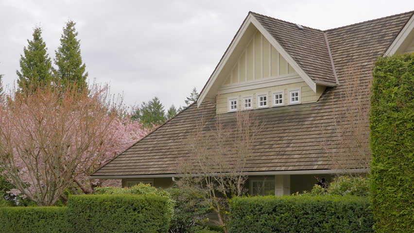 Establishing shot of two story stucco luxury house with garage door, big tree and nice spring blossom landscape in Vancouver, Canada, North America. Day time on Apr 2023. ProRes 422 HQ.