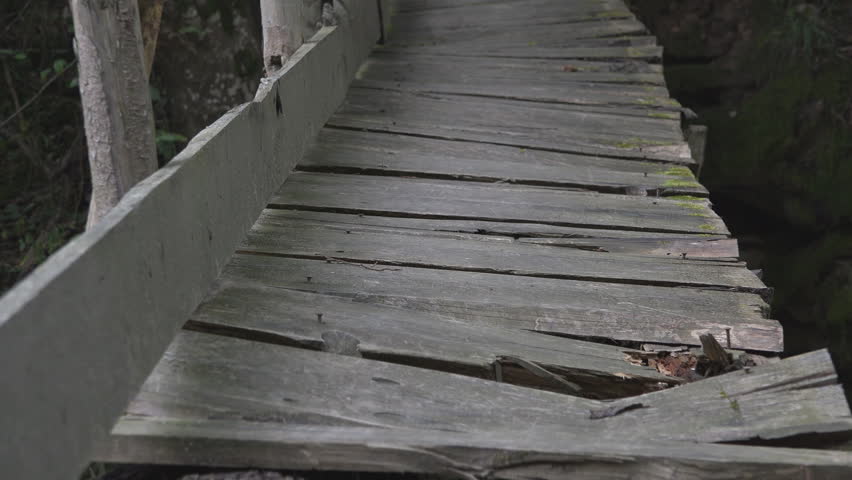 Old damaged rustic wooden bridge over a creek in the woods