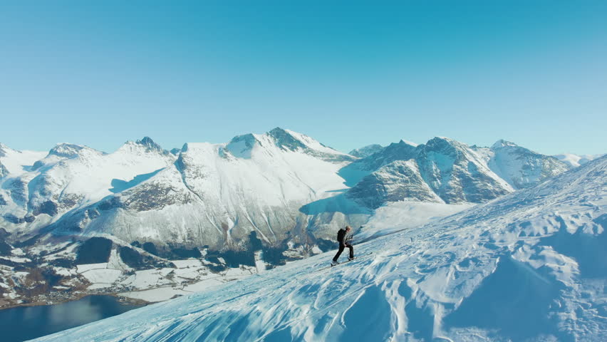Man goes uphill during ski touring adventure, hike up on randonee skis in epic norwegian fjord scenery. Inspiring epic adventure in winter landscape. Back country skiing and mountaineering 