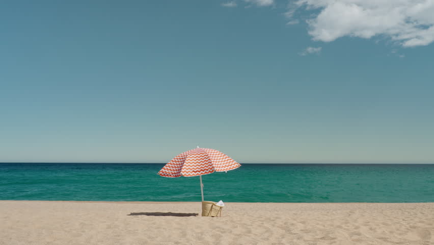 Cinematic minimalistic shot of idyllic paradise empty beach with sun umbrella and woven bag. Peaceful and quiet summer vacation concept. Holiday destination Royalty-Free Stock Footage #1103478771