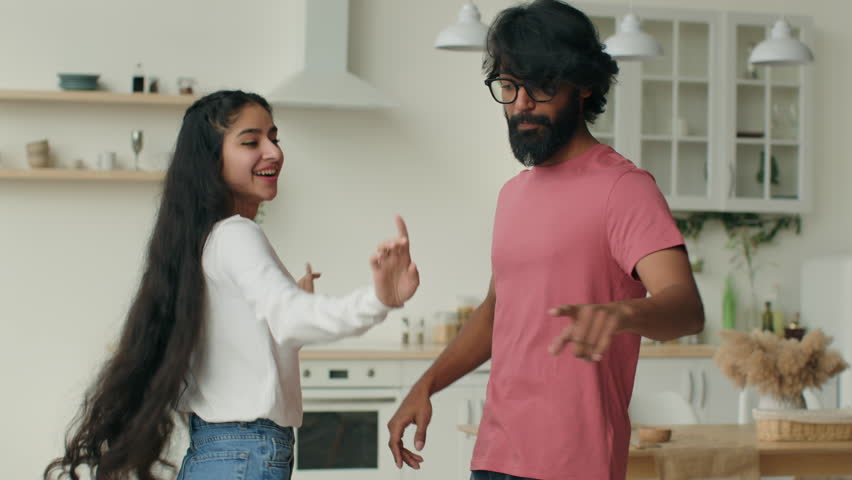 Arabian husband dance with indian wife happy carefree ethnic couple dancers dancing in home kitchen listen music smiling woman girl and man guy have fun celebrate weekend relocation to rented house Royalty-Free Stock Footage #1103483509
