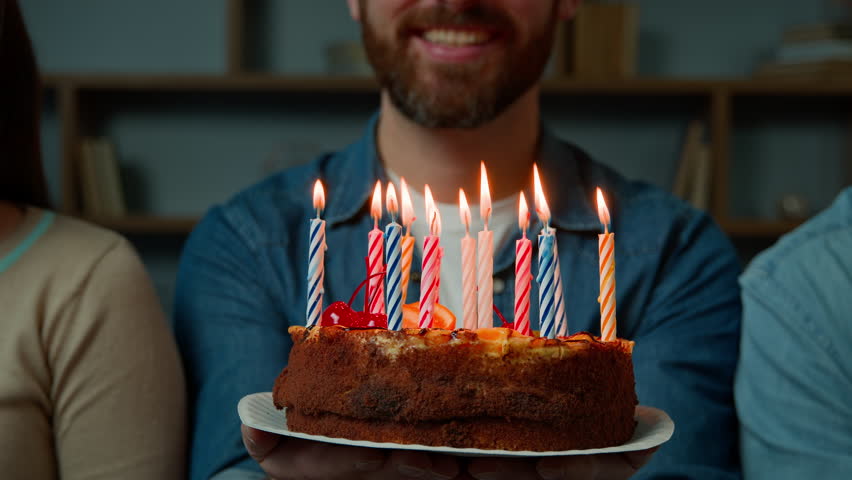 Close up festive cake with burning candles happy bearded unrecognizable birthday man smiling make wish celebrate event with friends at home party celebration anniversary year tradition congratulation Royalty-Free Stock Footage #1103483521