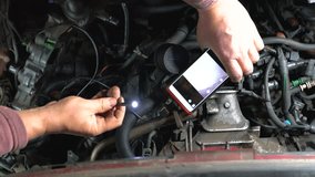 Hands of car mechanic check the vehicle engine with technical endoscope with rotary camera and mobile phone. Repair of engine head and valves.