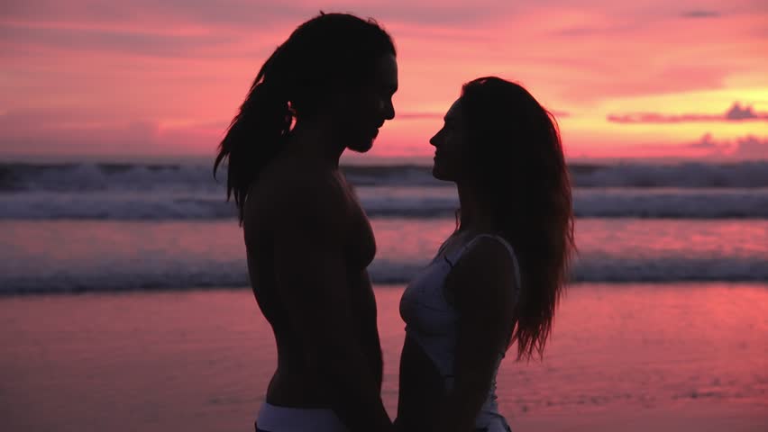 Lovely Couple Of Young Man And Happy Woman Kiss At Sea Beach Or Ocean Water. Romantic Lifestyle Of Sexy People In Swim Suits Bonding At Summertime Journey To Scenic Bay. Handsome Surfer Flirts To Lady