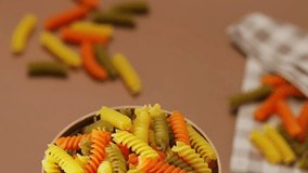 Raw colorful italian fusilli pasta on a beige background. Dry pasta in a cardboard box. Tilt down camera movement