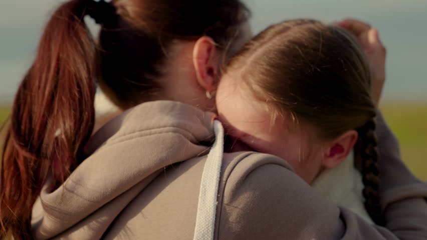 Child with tears in their eyes hugs their mother, emotionally. Child is crying in park in arms of mom. Mommy soothes baby. Family, mother, kid. Loving young mother hugs and soothes her little daughter Royalty-Free Stock Footage #1103492335