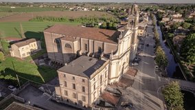 Breathtaking aerial footage of a bell tower and church in a charming Venetian village, surrounded by countryside at sunset.
