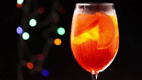 Glass of Aperol Spritz cocktail on a blurred background with colorful bokeh. Mixing Aperol Spritz with a cocktail spoon. Static shot