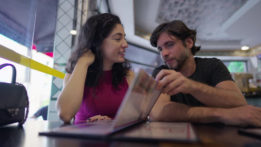 Happy couple looking at menu sitting inside restaurant. Man and woman together at table diner for lunch time