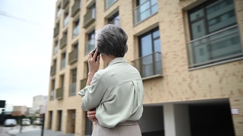 Mature caucasian woman talking on a smartphone in the street. The video rotates 360 degrees.
