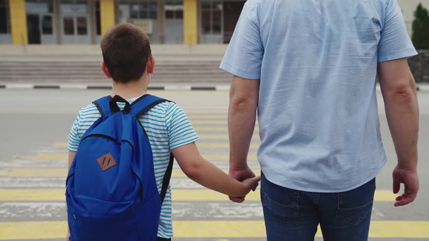 Child schoolboy with backpack his shoulders holds his father hand while crossing pedestrian crossing. Zebra road. traffic rules for children. student holding dad hand. Dangerous road traffic concept.