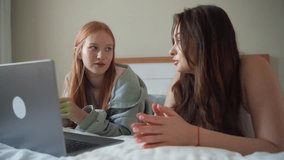 Two teenage girls having break at home using laptop, watch video film, social media, clip, reel. Young women talking, gossip, chitchat, having fun.