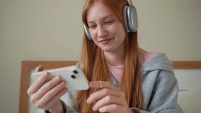 Teenage girl headphones using smartphone at home on bed. Young woman listen to music online podcast watch video with gadget, online chatting messaging with friends Internet technology, communication