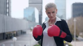 Businesswoman clashing boxing gloves and standing in guard position outdoors - Powered by Shutterstock - Get 15% off with code: PIKWIZARD15