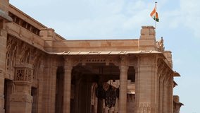 kingdom flag flowing at the top of palace entrance gate made of red stone at day from flat angle video is taken at umaid bhawan palace jodhpur india.