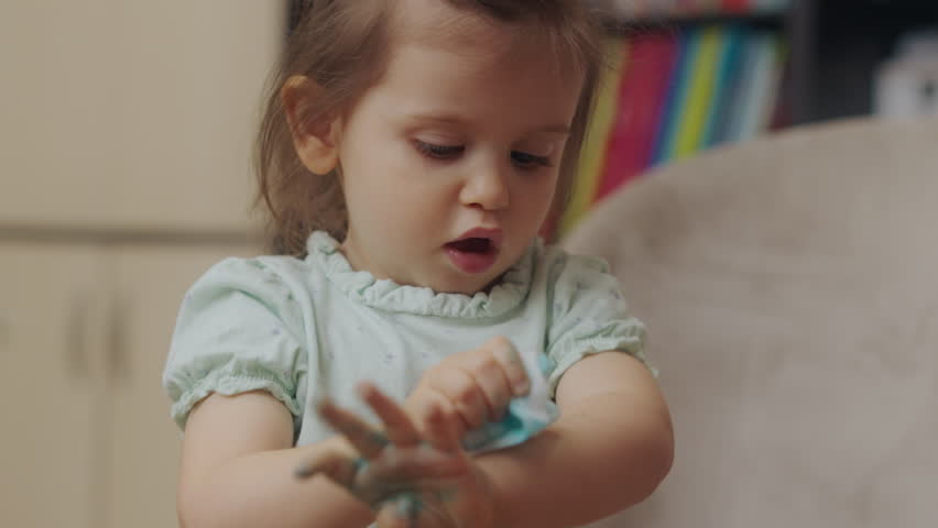 Baby girl wiping her dirty hands from the blue carioca with a wet napkin. Love concept. Happy family kid concept. Skin care. Royalty-Free Stock Footage #1103502771