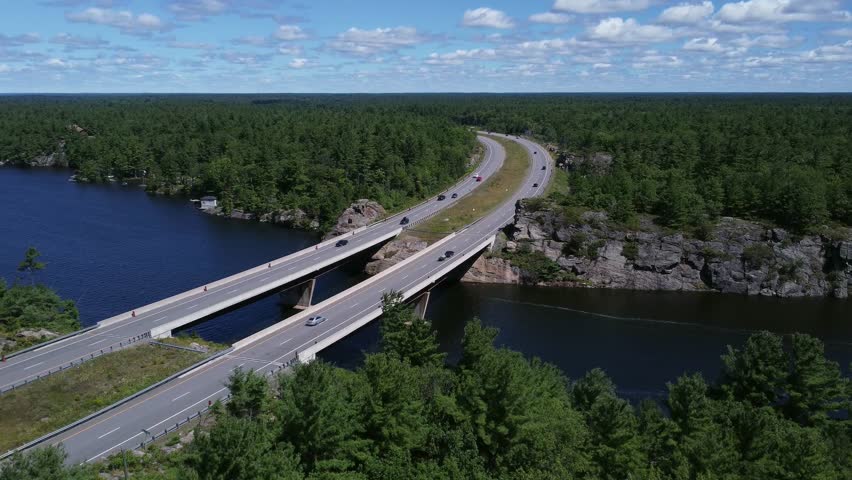 Rising aerial shot of curved highway bridge over lake through rock and trees near Gravenhurst Ontario