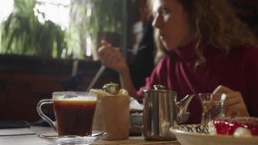 Woman is having lunch in a restaurant sitting near the window, the video is out of focus. She spreads the sauce on a slice of bread tortilla. Steam rises from a cup of coffee.