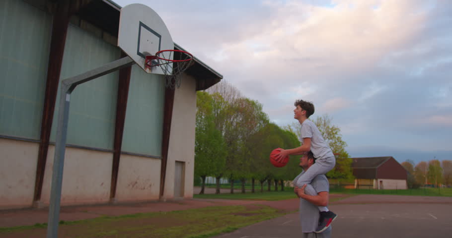 Dad teaches son to play basketball. Father helping son to throw a basketball into the basket. Father and son playing basketball