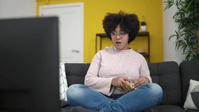 Young african american woman watching tv sitting on sofa eating chips at home - Powered by Shutterstock - Get 15% off with code: PIKWIZARD15