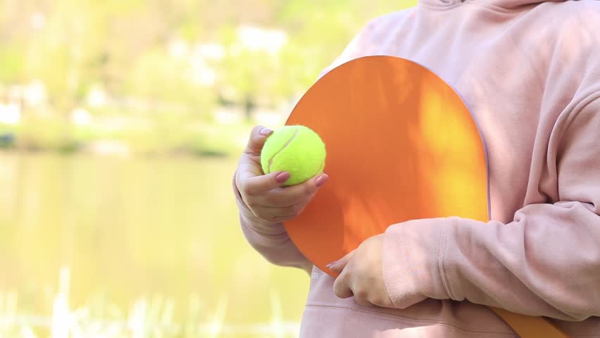 The player is holding a tennis racket. Waiting game in nature. Wooden tennis racket and ball in hand. Outdoor games near the lake