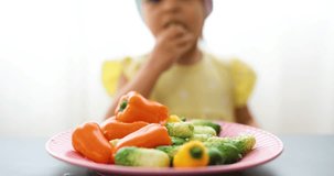 Little girl eats vegetables at a table in a bright room. Blurry video.