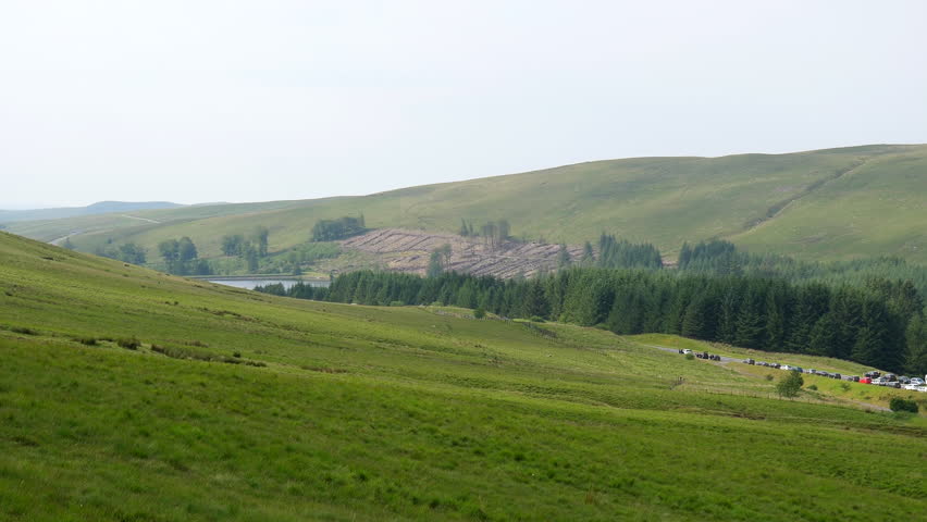 Handheld panning shot from hill of many vehicles parked on roadside of A470 road and in Pont ar Daf car park at the start of popular route to Pen y Fan peak in Brecon Beacons National Park in Wales.