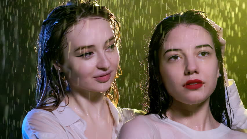 Young woman makes girl friend with vivid lips laugh stroking on wet hair. Tender ladies stand and laugh under night cold rain