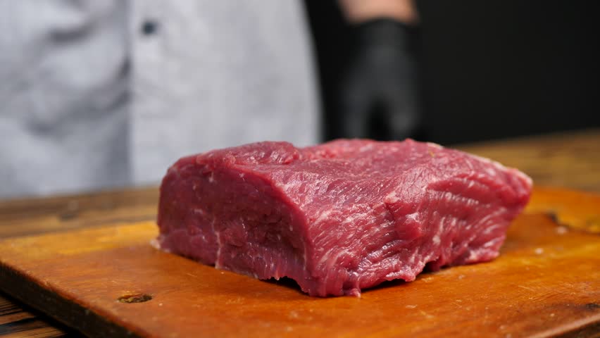 A butcher in gloves cuts a carcass of red meat.Close-up of a professional knife cutting a huge piece of meat in a butcher's shop on a cutting board Royalty-Free Stock Footage #1103527905